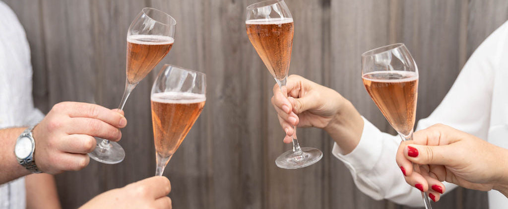 Four people holding champagne glasses in a celebratory manner against a wooden background.